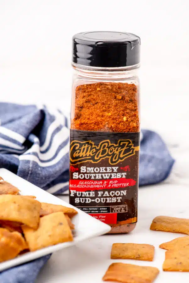 A container of smokey southwest seasoning beside a plate of sourdough chips.