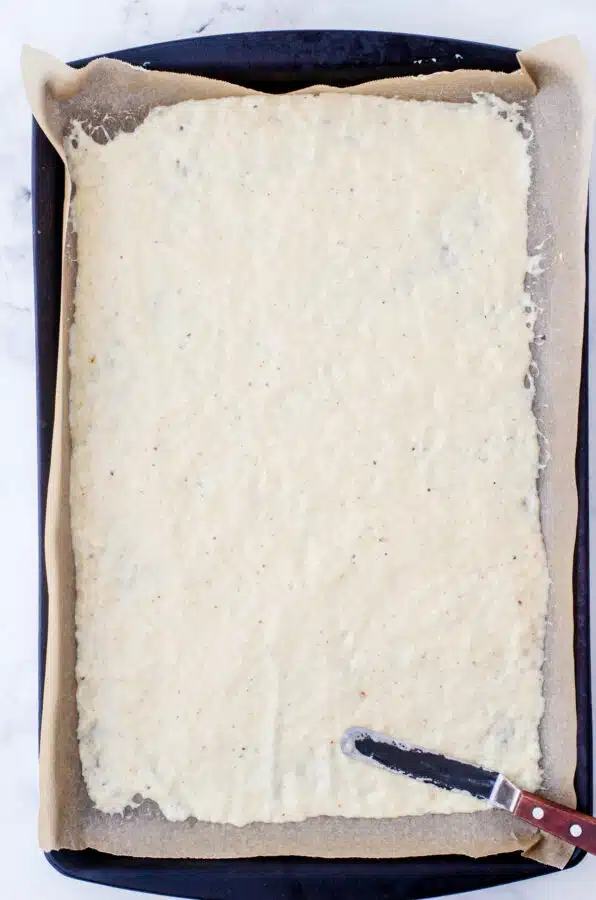 Sourdough discard and spices spread thinly on a parchment lined baking pan for sourdough crackers.