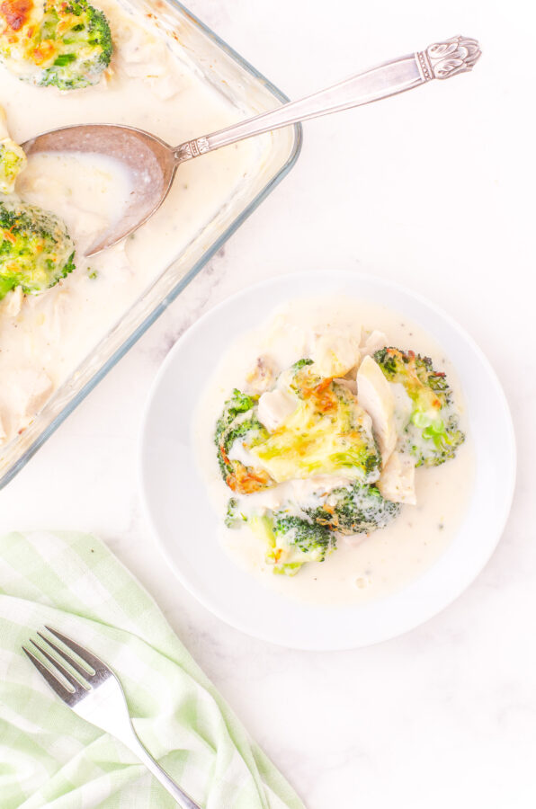 A serving of baked broccoli chicken alfredo on a plate with the casserole beside it.