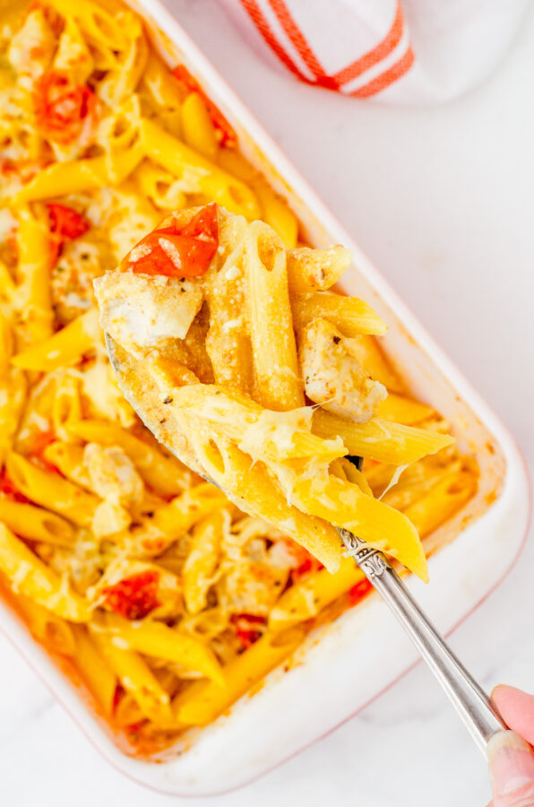 A serving spoon with feta chicken pasta on it with the pan of it in the background.