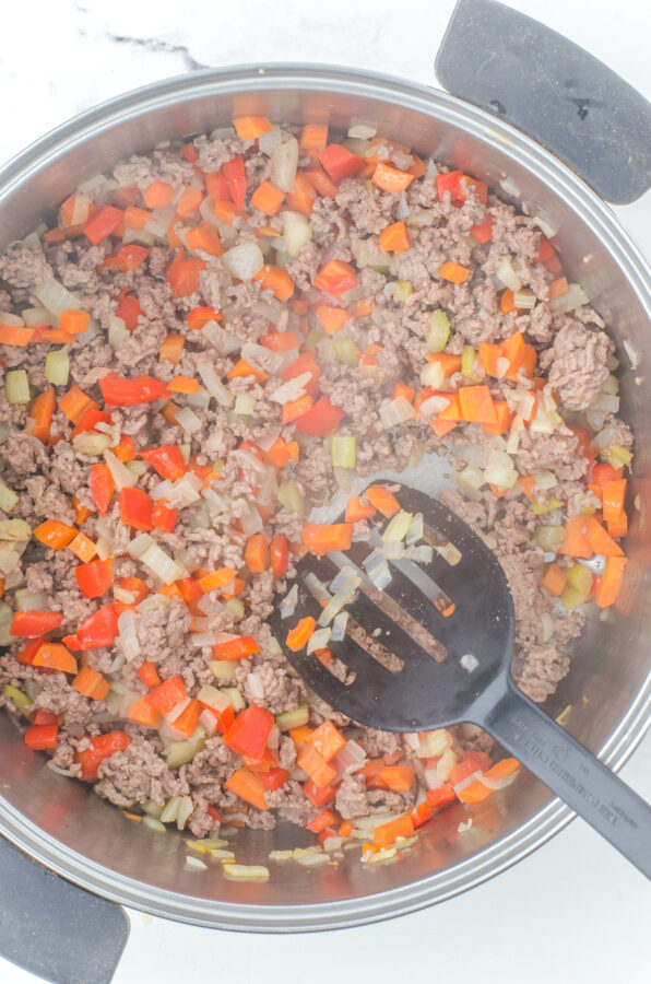 Browned ground beef and sauted vegetables in a large stockpot for hamburger rice soup.