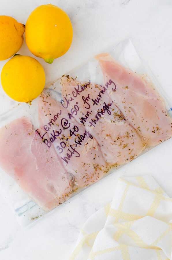 Lemon Chicken marinade in a marked ziptop bag with chicken breasts and marinade inside with lemons sitting above it.