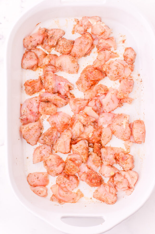 Diced chicken coated in spices in the bottom of a baking dish.