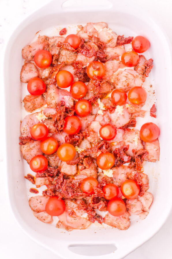 Cherry tomatoes and sundried tomatoes scattered over the top of diced chicken in the baking dish.