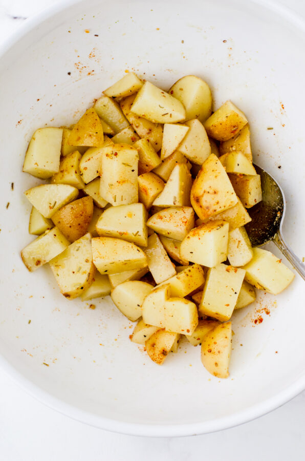 Diced potatoes in a mixing bowl that have been tossed with olive oil and spices.
