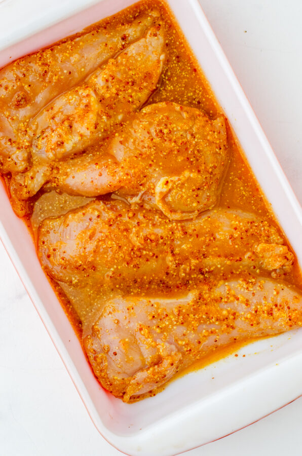 Chicken with marinade in a baking dish.