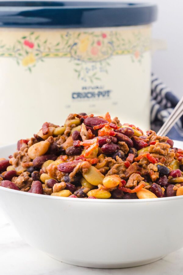 A serving dish full of crock pot baked beans with a crock pot behind it.