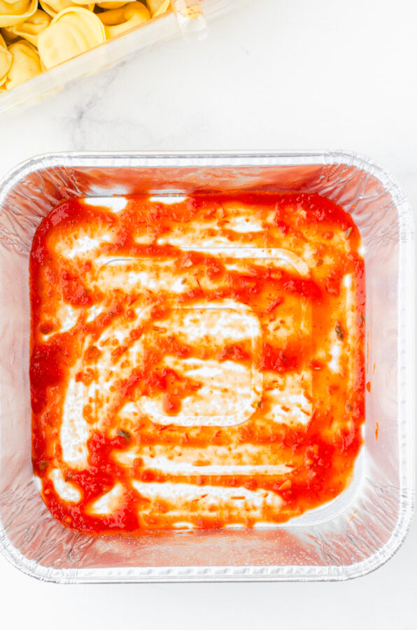 Thin layer of marinara sauce on the bottom of a pan for tortellini and sausage casserole
