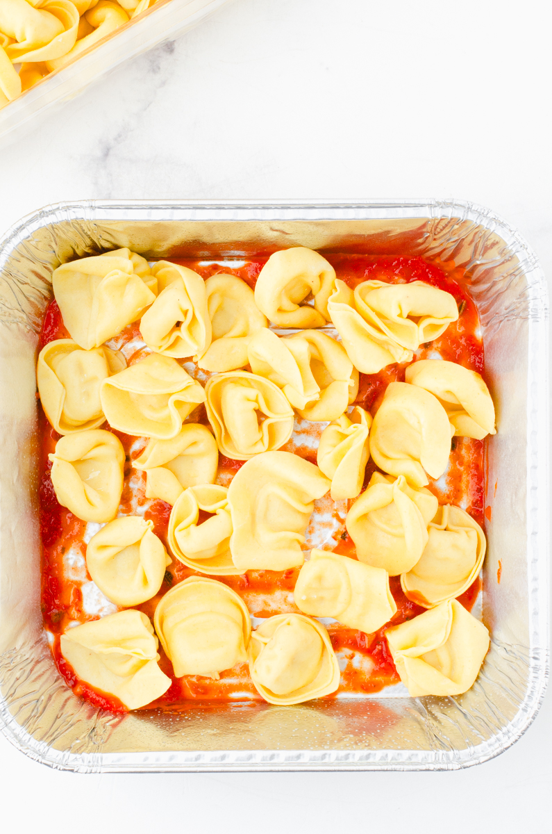 A single layer of cheese tortellini over the marinara sauce in a square pan