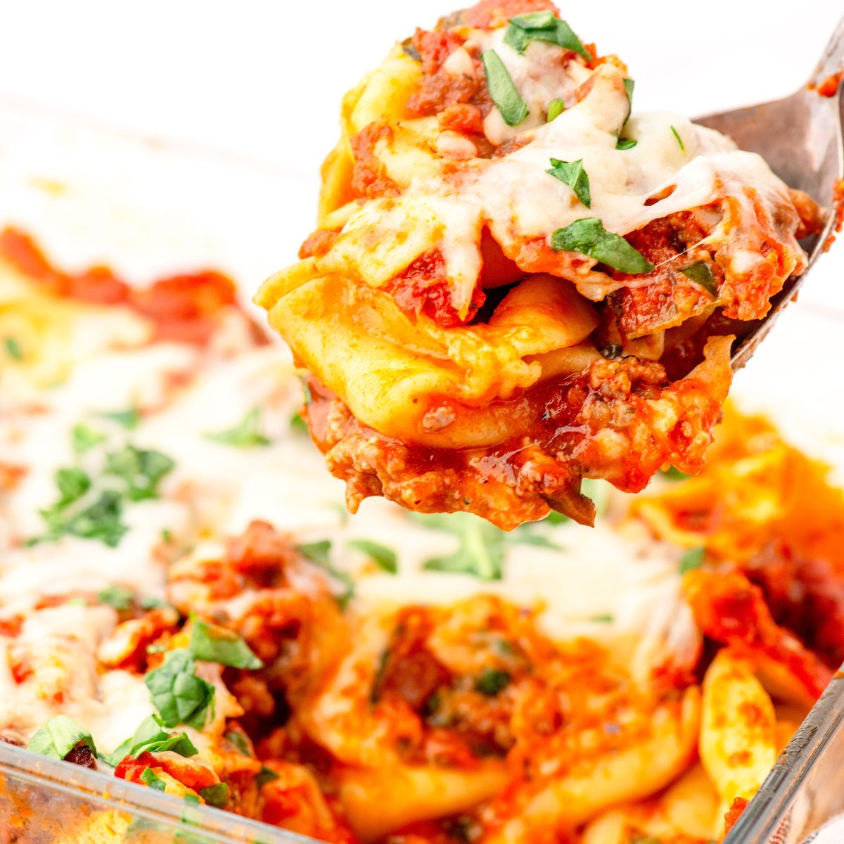 A serving spoon full of sausage and tortillini casserole bake