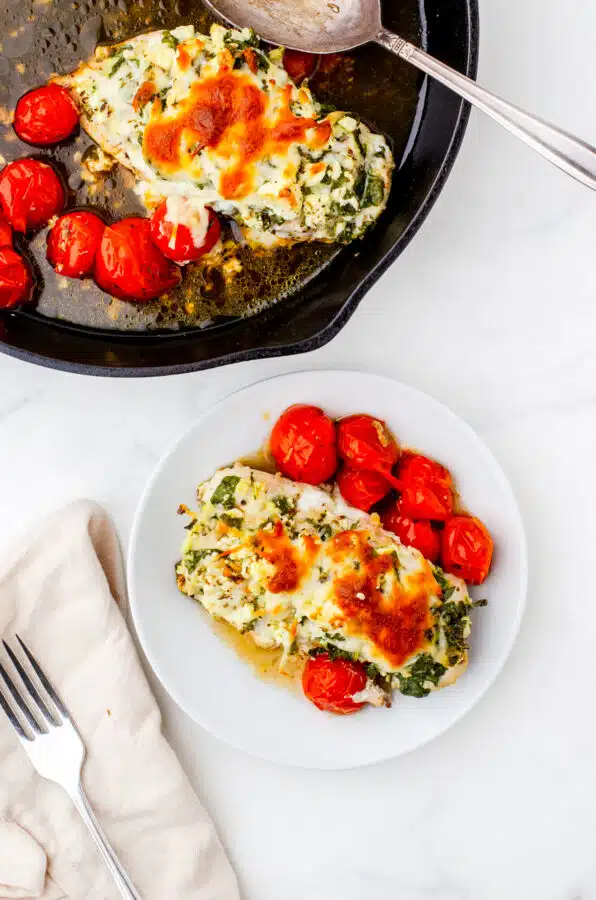 Spinch & feta hasselback chicken on a plate with baked grape tomatoes beside it.