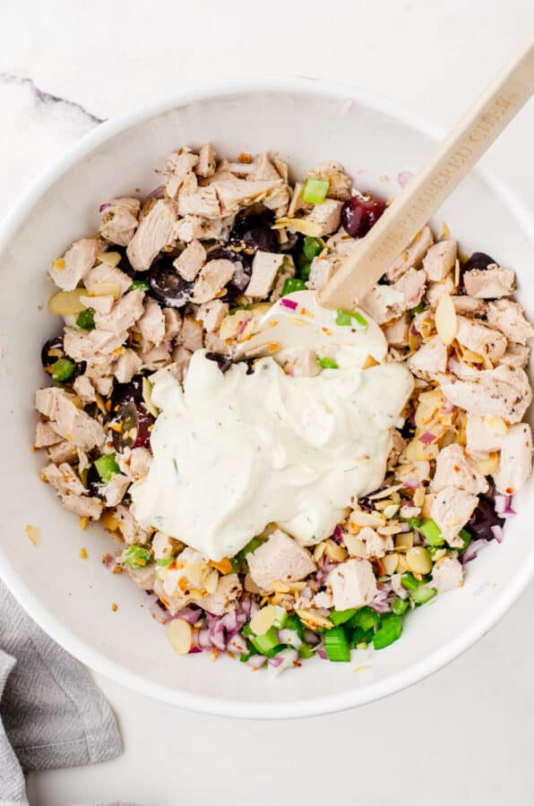 Chicken salad dressing being added to chicken salad ingredients in a mixing bowl.