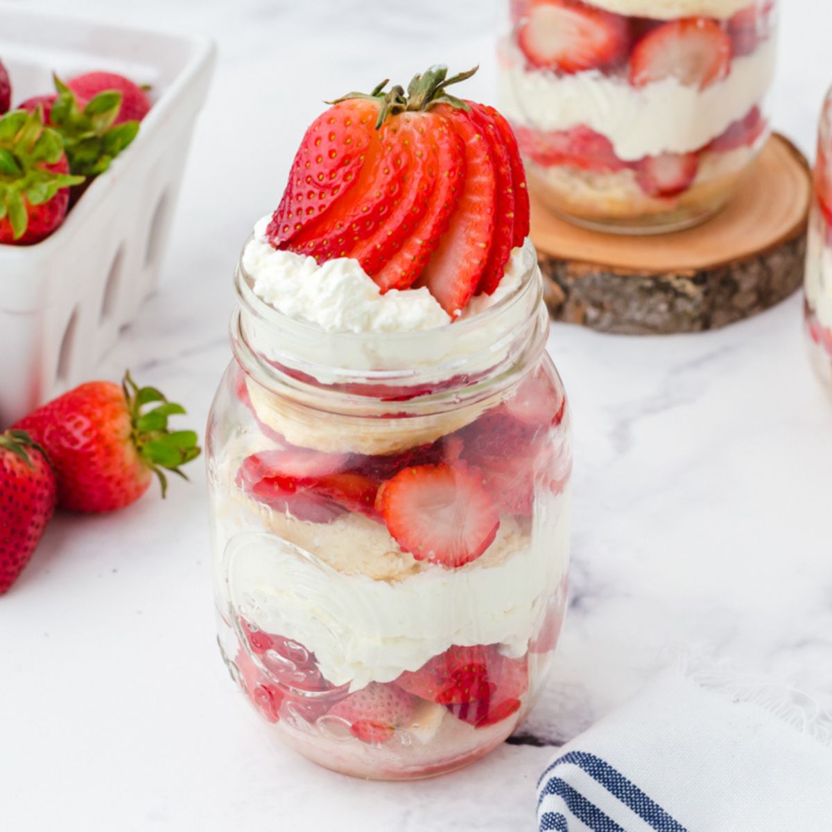 Strawberry shortcake with whipped cream and sliced strawberries layered in a mason jar