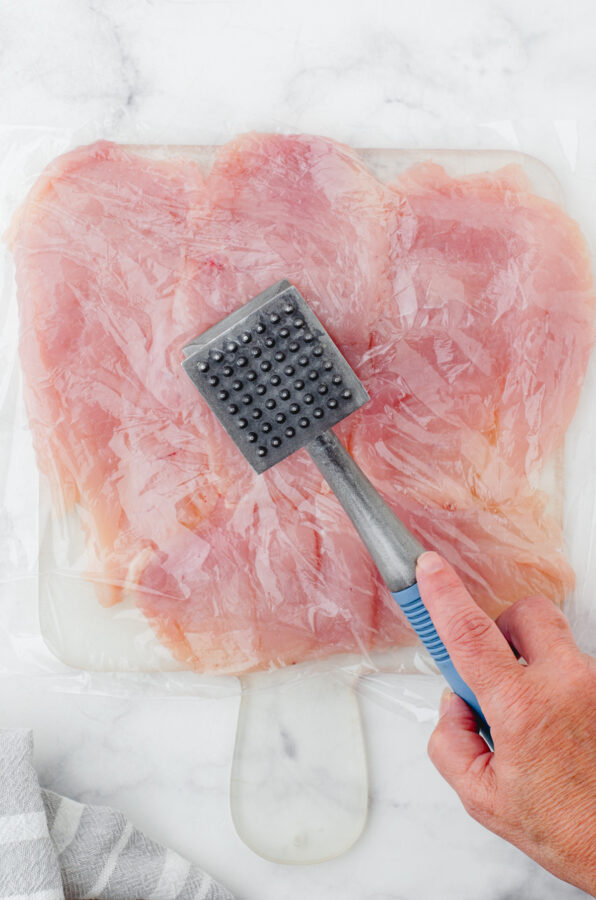 Pounding chicken breasts with a meat mallot to make them thin.