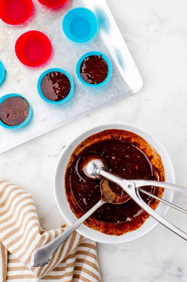 Almond butter chocolate cups being scooped into silicone mini muffin cups