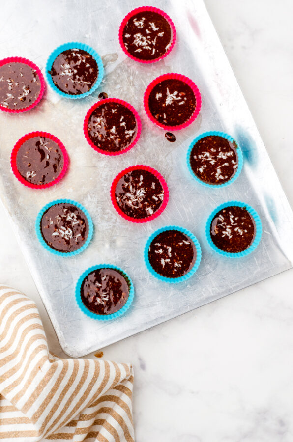 Mini muffin silicone cups filled with almond butter chocolate cups mixture ready to be put in the freezer on a cookie sheet.