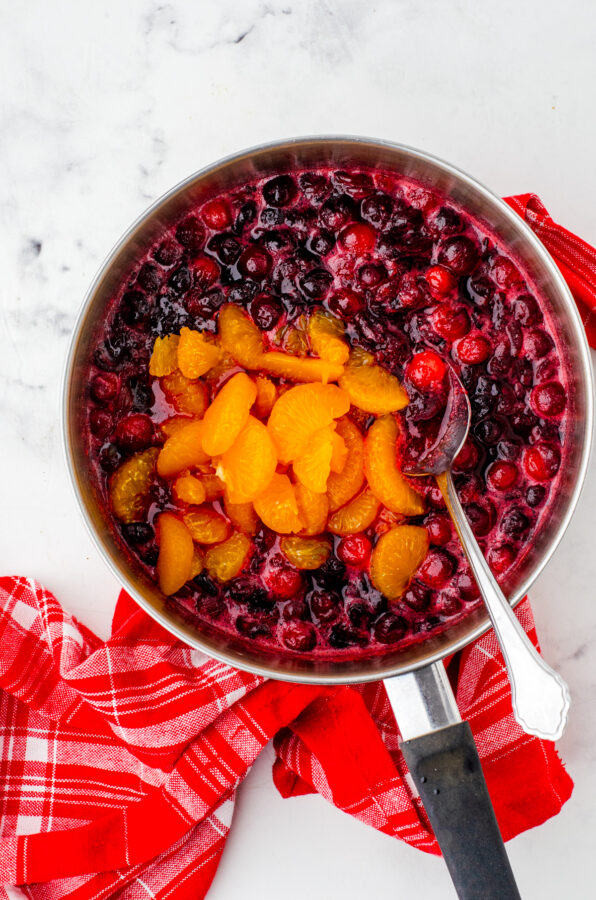 Mandarin oranges being added to partially cooked cranberries in a saucepan