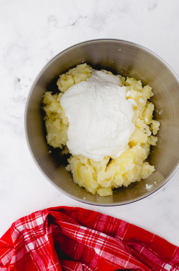 Pureed cottage cheese on partially mashed potatoes in a mixing bowl.