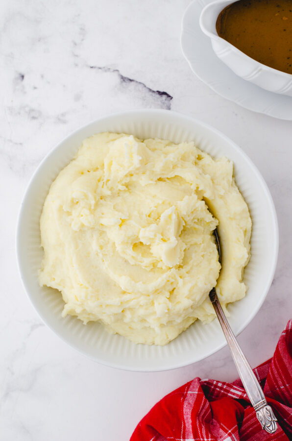 Whipped potatoes in a serving bowl with gravy beside.