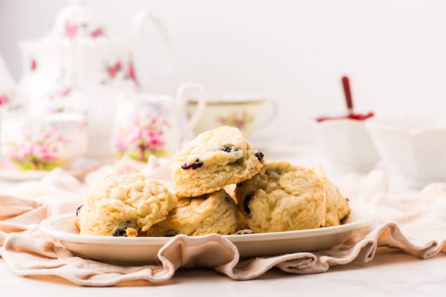 A platter of cream scones with cranberries and orange peel with a teapot behind