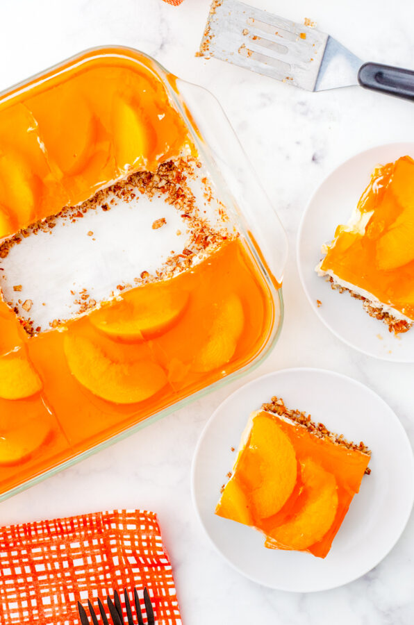 A pan of peach pretzel salad with two pieces cut out and on dessert plates.