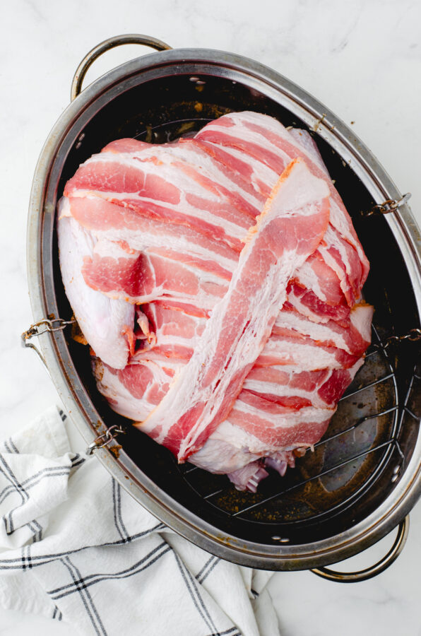 Whole turkey in roasting pan covered with strips of bacon