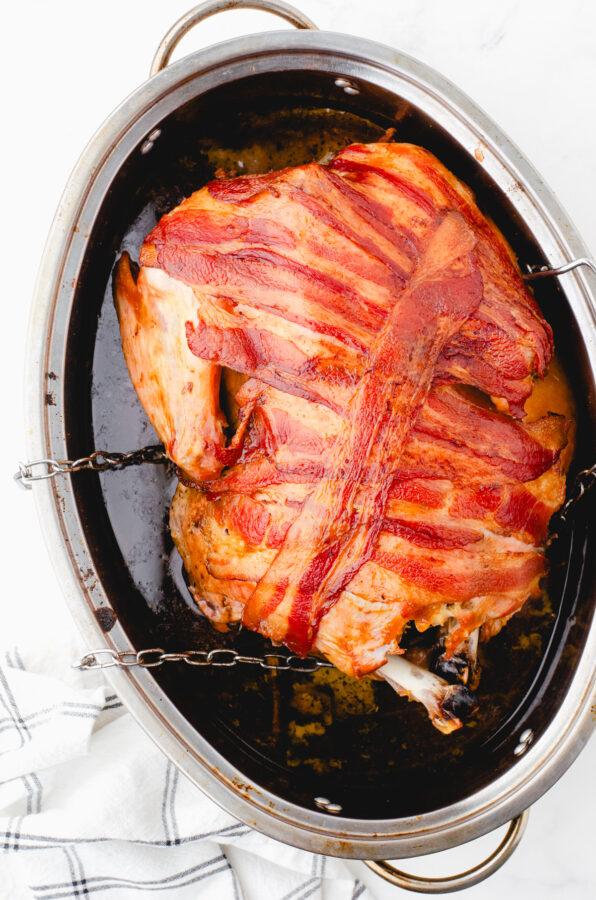 Roasted whole turkey with crispy bacon covering it in a roasting pan.