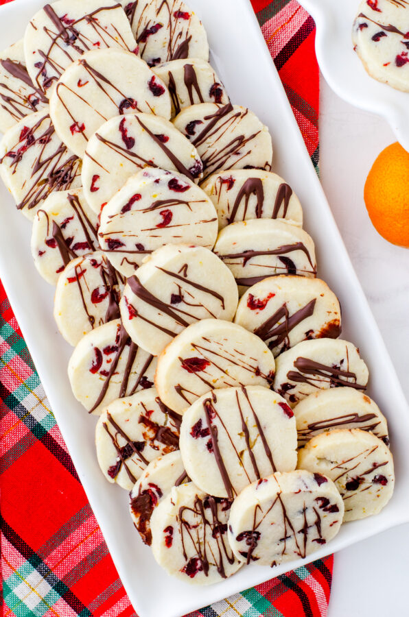 A platter of slice and bake whipped shortbread cookies with cranberries and a chocolate drizzle.