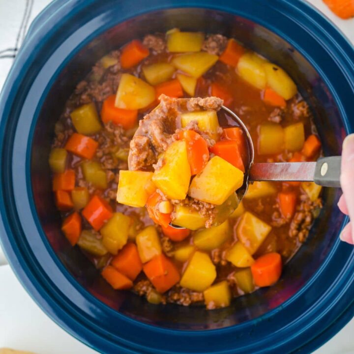 a ladle full of hamburger stew being served out of a crock pot